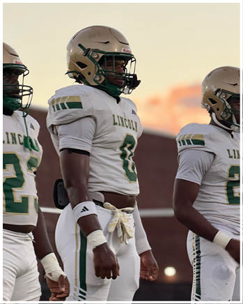 Two people wearing football helmets and white jerseys with the word Lincoln and numbers stand side by side outdoors during sunset. Description generated by AI