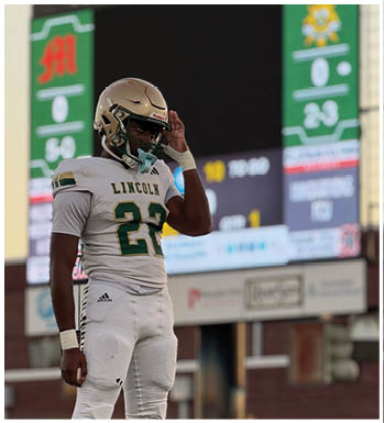 A person wearing a football uniform with the number 22 and a helmet stands on a field with a scoreboard in the background. Description generated by AI