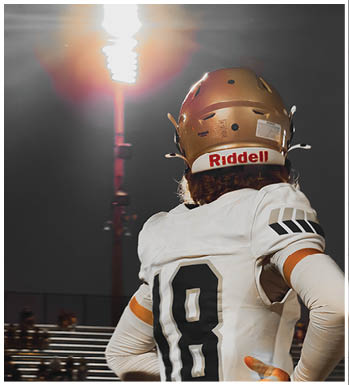 A person wearing a football helmet and white jersey with the number 10 is standing under bright stadium lights at night. Description generated by AI