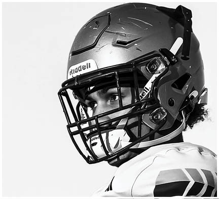 A person wearing a football helmet and jersey is looking to the side in a black and white photo. Description generated by AI