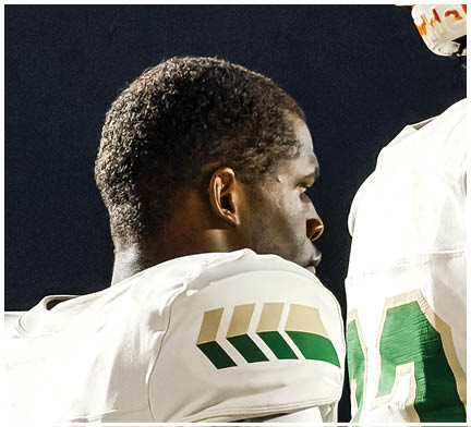 Two people wearing white sports uniforms with green and gold accents are standing close together against a dark background. Description generated by AI
