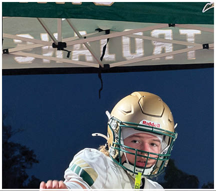 A person wearing a gold football helmet and white jersey is preparing to throw a football under a tent at night. Description generated by AI