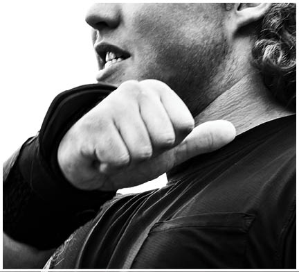 A person wearing a dark shirt is shown from the neck to the chest with a clenched fist raised near their face in a black and white close-up photograph. Description generated by AI