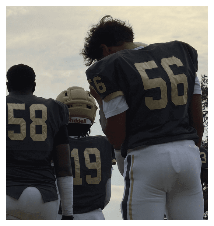 A person wearing a dark sports jersey with the number 56 is standing next to another person wearing a helmet and a similar jersey. Description generated by AI