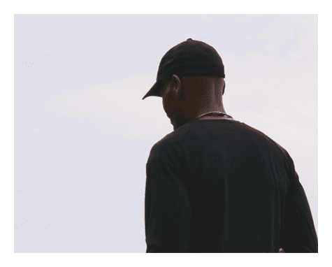 A person wearing a black cap and dark clothing is seen from behind against a pale sky background. Description generated by AI