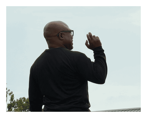 A person wearing glasses and a black long-sleeve shirt is seen from behind against a clear sky while raising one hand with fingers slightly bent. Description generated by AI