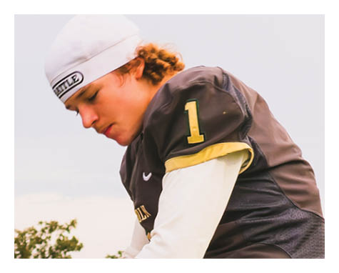 A person wearing a white cap and a dark sports jersey with the number one is looking down thoughtfully outdoors. Description generated by AI