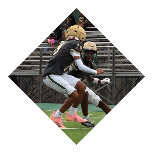 Two people wearing sports uniforms and cleats are engaged in a football play on a green field with white yard lines. Description generated by AI