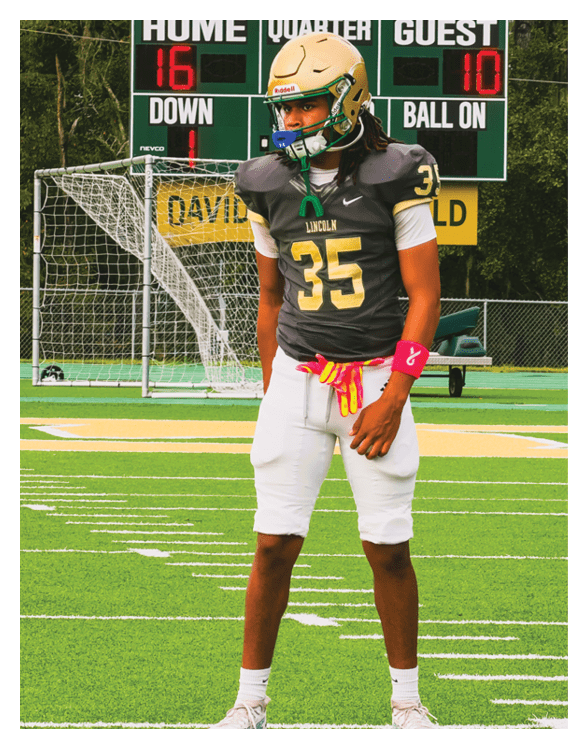 A person wearing a football uniform with the number 35 stands on a football field with a scoreboard and goalpost in the background. Description generated by AI