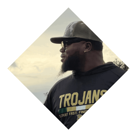 A person wearing a camouflage cap, dark sunglasses, and a dark shirt is shown in profile against a cloudy sky. Description generated by AI
