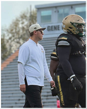 People wearing sports attire are on a field with bleachers in the background, and one person in a white long-sleeve shirt and cap is standing near the bleachers. Description generated by AI