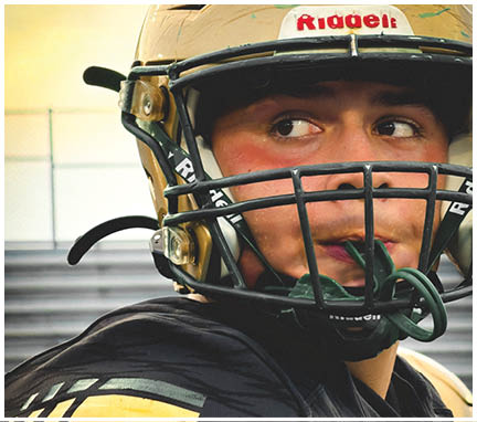 A person wearing a black football jersey with shoulder pads and a green helmet is shown from the chest up. Description generated by AI