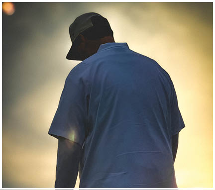 A person wearing a blue shirt and dark pants is standing with the sun shining brightly behind them. Description generated by AI