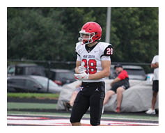 A person in a football uniform stands on a field while two people in casual clothing stand in the background near covered objects. Description generated by AI