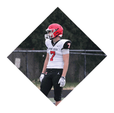 A person wearing a red helmet, white jersey with the number seven, and black pants is standing on a football field. Description generated by AI