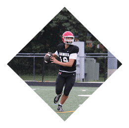 A person wearing a red helmet and black sports uniform is running on a football field while holding a football, preparing to throw it. Description generated by AI