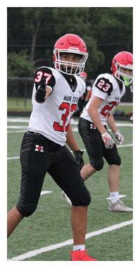 Several people in football uniforms and helmets stand on a field preparing for a play, with one person in the foreground pointing forward. Description generated by AI