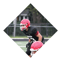 Three people wearing red helmets and football uniforms are positioned on a football field, appearing ready for a play. Description generated by AI