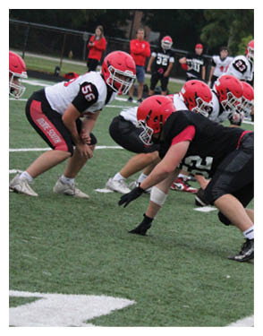 People in sports uniforms are lined up on a football field preparing for a play. Description generated by AI