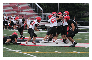 People wearing sports gear are engaged in a football game on a field with marked lines and a large red and white logo. Description generated by AI