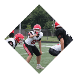 Several people wearing red helmets and sports uniforms are positioned on a football field preparing for a play. Description generated by AI