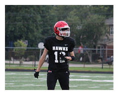 A person wearing black athletic pants and shoes is standing on a green sports field with white and yellow lines near a large red and white logo. Description generated by AI