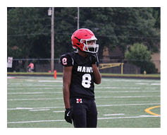 A person wearing a red helmet and black football uniform with the number 8 stands on a green football field with a referee walking in the background. Description generated by AI