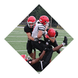 Three people wearing football uniforms and helmets are engaged in a tackle on a green football field. Description generated by AI