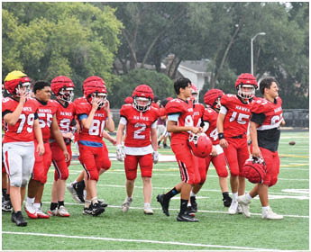 A group of people wearing red and white football uniforms are walking together on a green football field. Description generated by AI