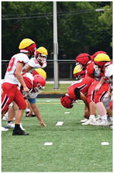 People wearing football helmets and uniforms are lined up on a field facing each other, preparing for a play. Description generated by AI