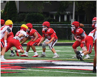Several people wearing red and white football uniforms and helmets are engaged in a play on a green football field. Description generated by AI