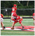 Children wearing red football uniforms and helmets are positioned on a football field preparing for a play. Description generated by AI