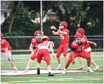 Five people in red and white football uniforms are positioned on a field, appearing ready for a play during a game. Description generated by AI