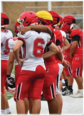 People wearing football helmets and uniforms are standing close together, with one person’s arm around another. Description generated by AI
