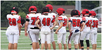 A group of people wearing white and red football uniforms stand in a line on a grassy field. Description generated by AI