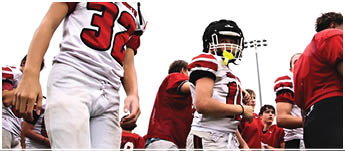 People wearing football uniforms and helmets are standing outdoors, likely preparing for a game or practice. Description generated by AI