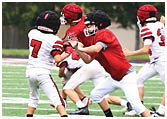 People wearing helmets and football uniforms are engaged in a play on a football field. Description generated by AI