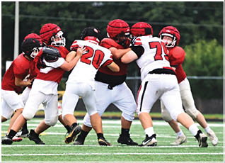 Children wearing helmets and football uniforms are engaged in a blocking drill on a grassy field. Description generated by AI