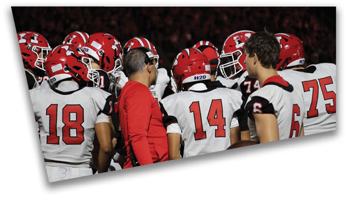 A group of people wearing red and white football helmets and uniforms are gathered closely around a person in a red shirt who appears to be giving instructions. Description generated by AI