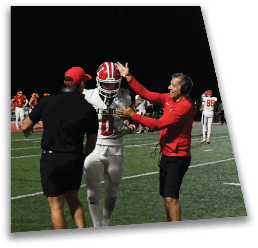 A person in a football uniform is walking on a field at night while two people in casual sportswear enthusiastically interact with them. Description generated by AI
