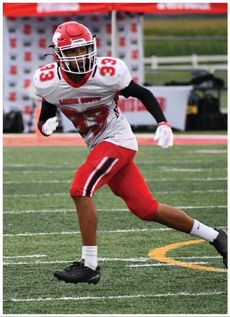 A person wearing a red and white football uniform with the number 33 is running on a field with a black and red tent in the background. Description generated by AI