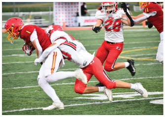 Two people in football uniforms are engaged in a tackle on a grassy field during a game. Description generated by AI