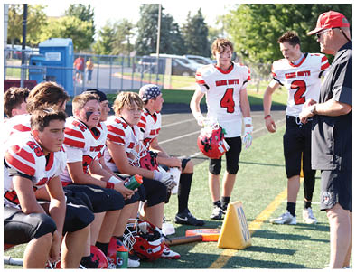 People wearing sports uniforms and cleats are sitting on a bench on the sidelines of a sports field with water bottles and equipment nearby. Description generated by AI