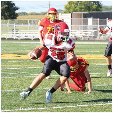 People in football uniforms are actively playing on a field with one person running with the ball while others are attempting to tackle or block. Description generated by AI