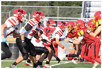 Two teams in red and white football uniforms are lined up facing each other on a field, preparing for a play. Description generated by AI