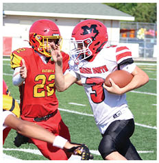 A person in a white and red football uniform is running with the ball while two people in red and yellow uniforms attempt to block or tackle on a sunny football field. Description generated by AI