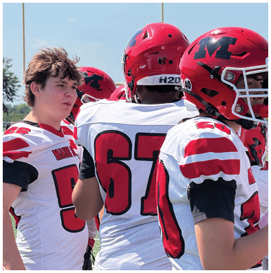 People wearing white and red sports jerseys are gathered closely together, likely participating in a team activity outdoors. Description generated by AI