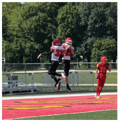 Two people in red and white football uniforms are jumping and celebrating on a football field while another person in a red uniform walks nearby. Description generated by AI