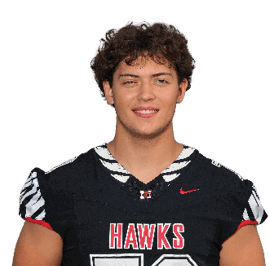 A person with curly hair is wearing a black sports jersey with the word “HAWKS" in red and white letters and smiling against a white background. Description generated by AI