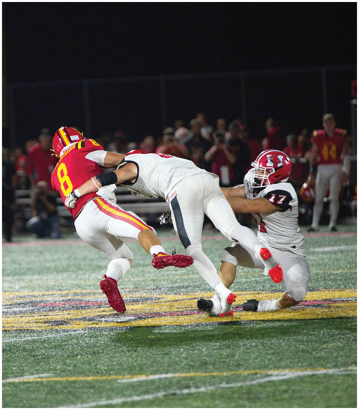 A person in a red and yellow football uniform is being tackled mid-air by two people in white and red football uniforms on a field at night. Description generated by AI